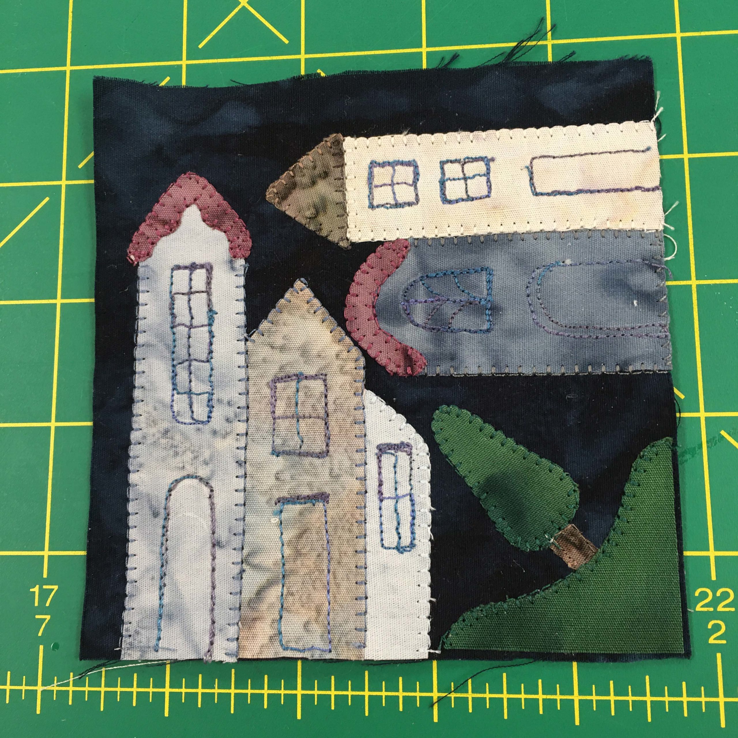 A quilt block on a green background depicting townhouses and a tree. The tree is in the corner, while the townhouses are both vertical and horizontal as if built on a corner.