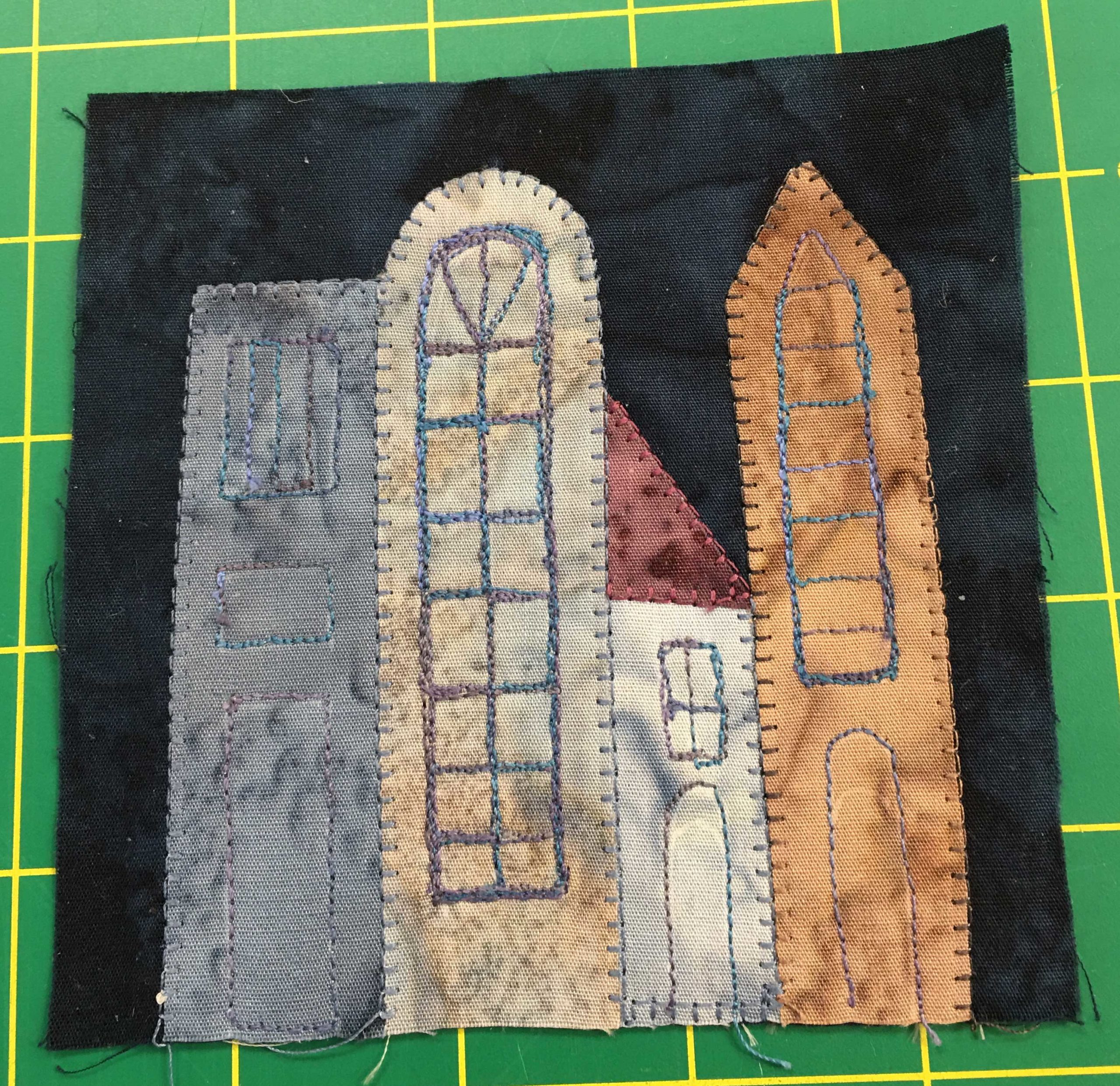 This quilt block shows four condo and apartment like buildings next to each other under a dark, near black night sky.
