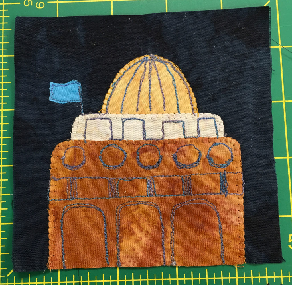 A grand building on a quilt block featuring a gold dome on top.