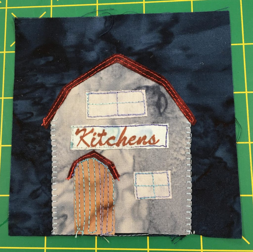 A quilt block showing a barn like building under a dark sky. It ks labeld