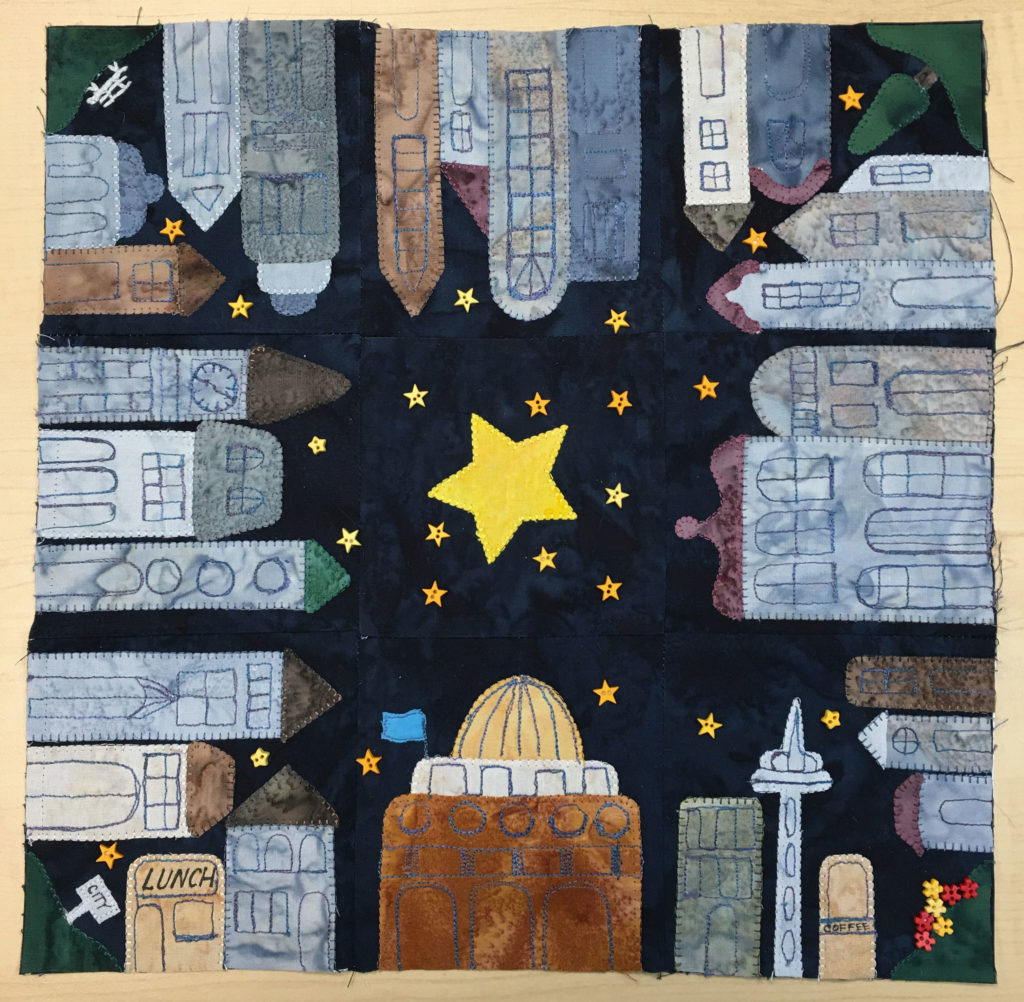 Nine quilt blocks are stitched together in a square. A star is in the center, and large number of tall buildings surround it pointing towards it. They form a city bock amongst many little star buttons.