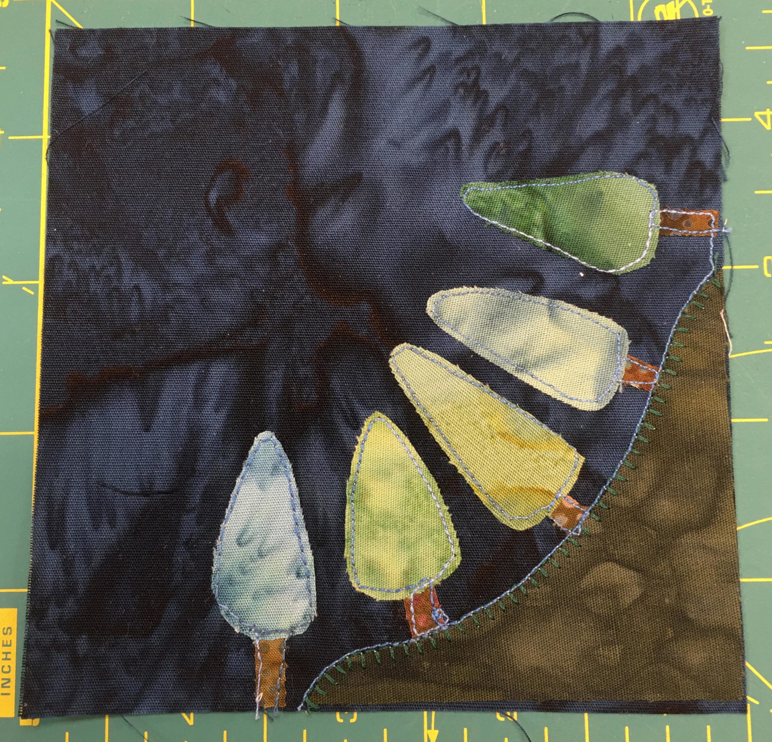 This quilt block depicts a green trees of various shades on a dark green mound in the bottom right corner. They angle from the bottom to the left.
