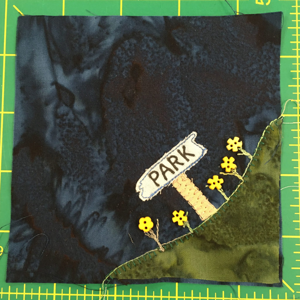 This quilt block shows a patch of grass in the bottom right corner with a sign that reads