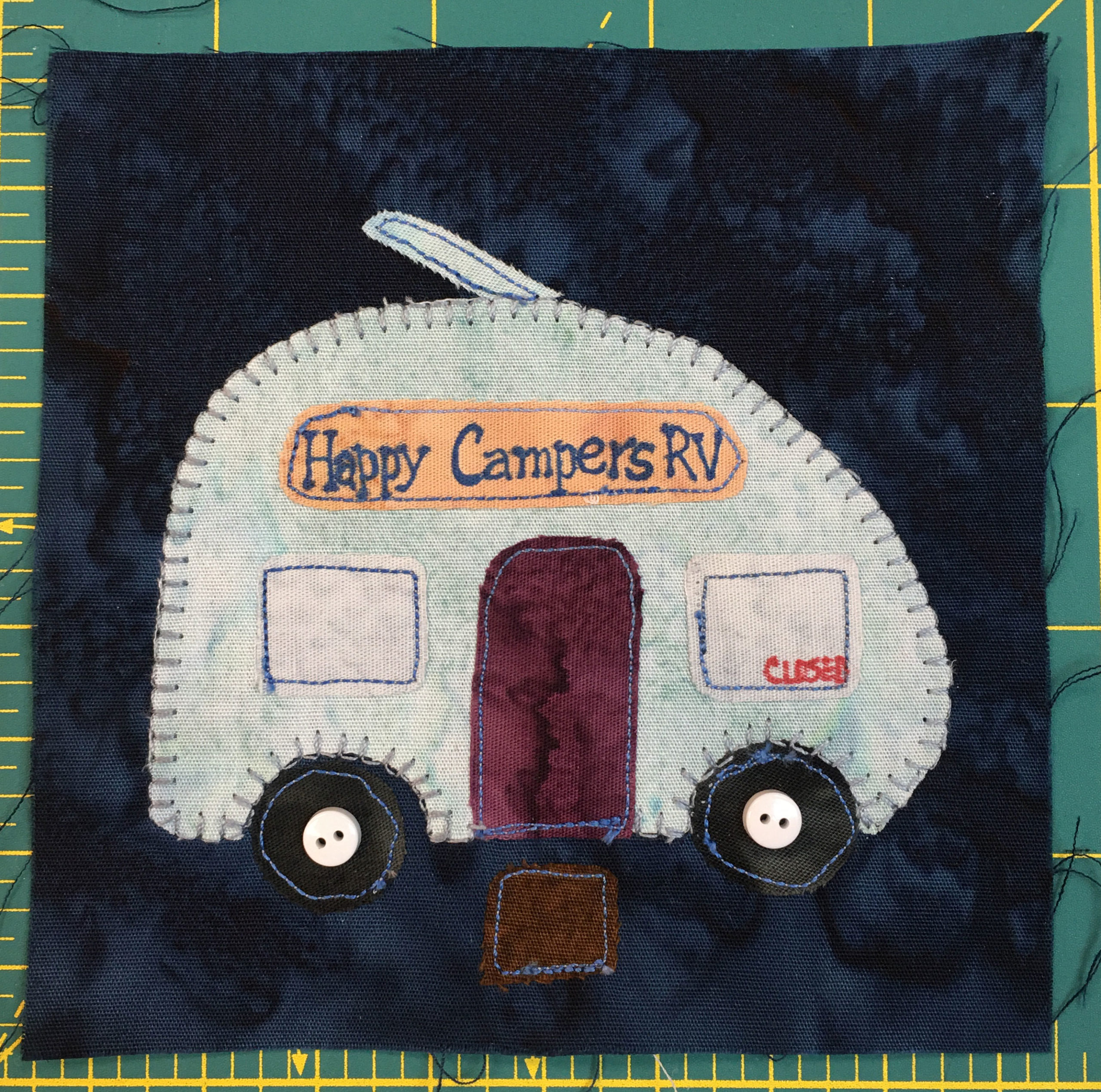 This quilt block shows an RV camper with a sign on it reading,