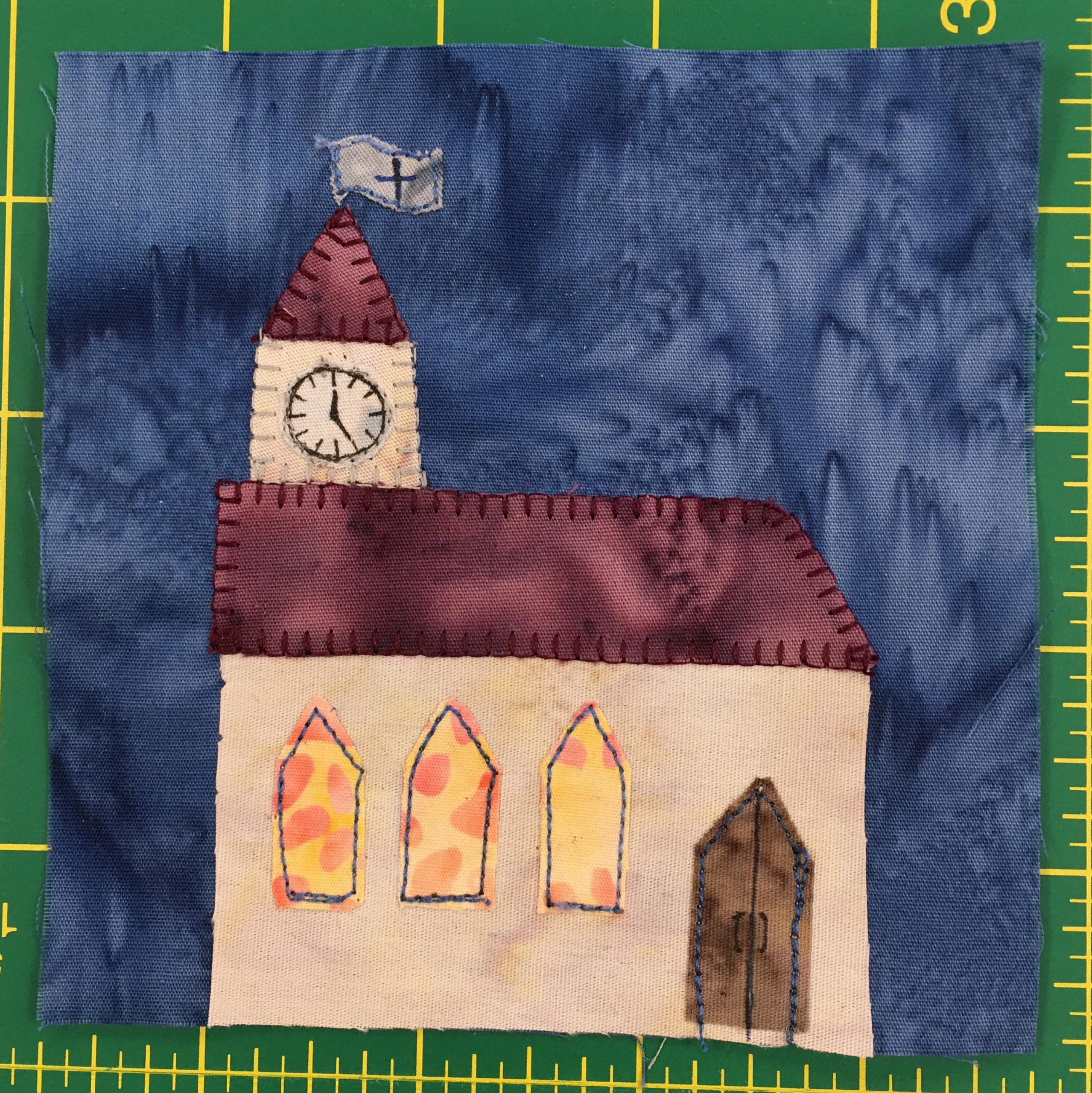 This quilt block shows a church with a steeple on the left. On the steeple is a clock. The church windows are a splotchy yellow-orange fabric indicating stained glass windows.