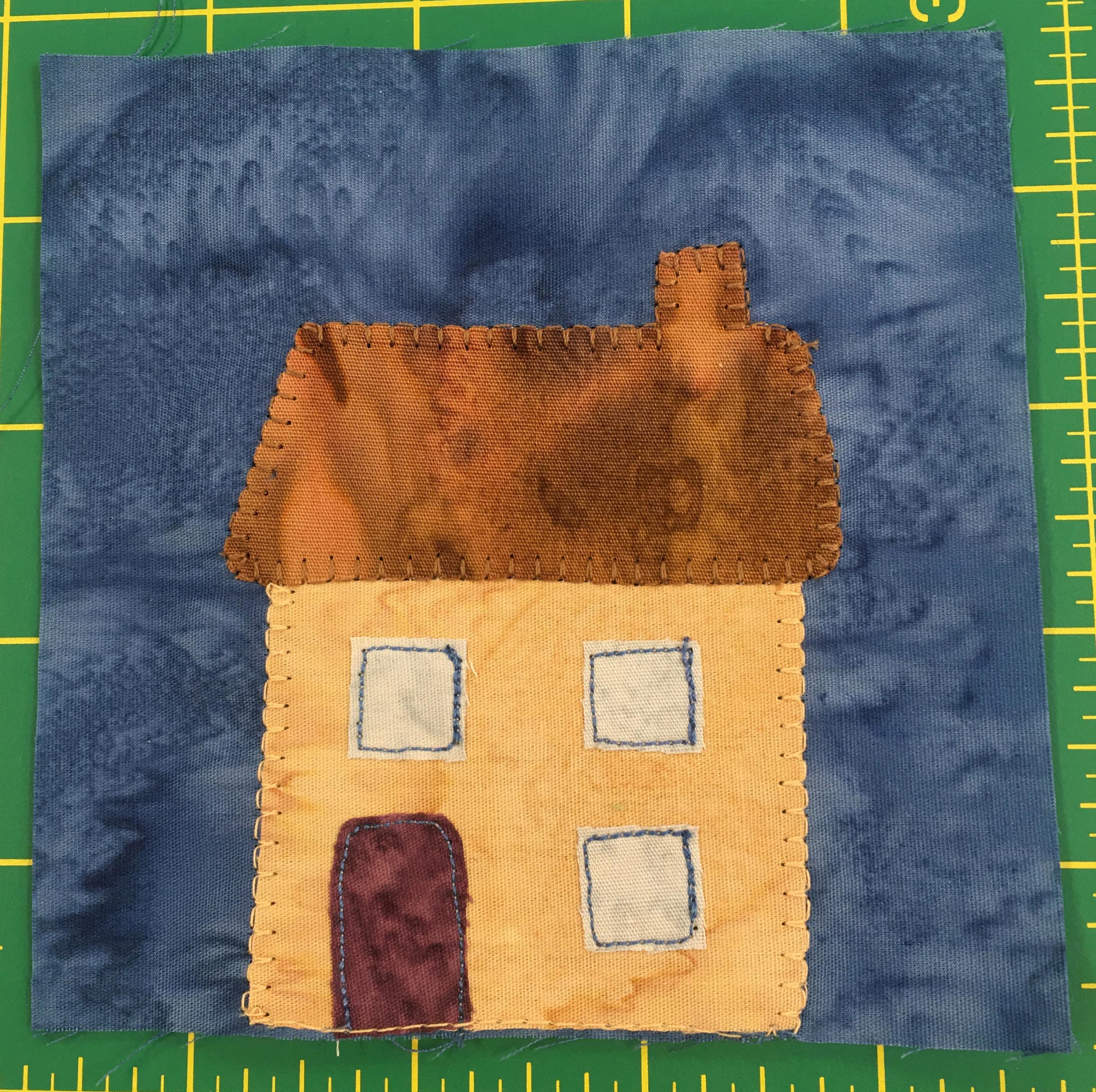This block shows a simple two story yellow house with three square windows, one below and two above. There is a maroon door on the left, and a brown roof with a chimney on the right.