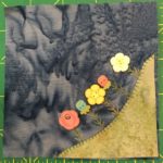 This quilt block shows a corner block with a patch of grass in the lower right corner. Poking out of the grass and towards the center of the block are several very detailed flowers of various kinds and colors. The detail of each flower bloom stands out in this block; the blooms themselves being medium sized flower pattern buttons.