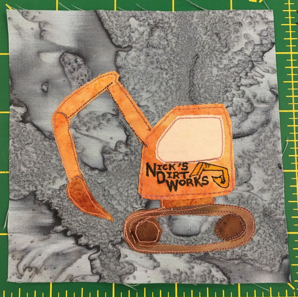 This quilt block depicts an pretty detailed orange excavator. On the side of the excavator door are the words,