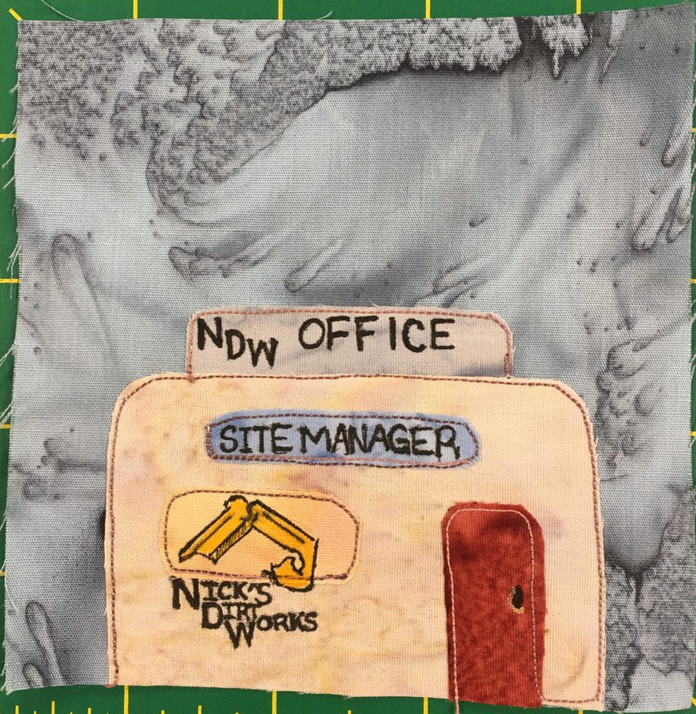 This quilt block shows a small office building against a light gray background. The building looks like a temporary construction office with a sign sticking out of the top of the roof that reads,