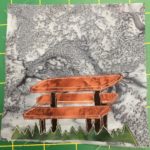 This quilt block shows a patch of grass at the bottom using a jagged cut of green fabric. On top of the grass is a rather three-dimensional looking brown picnic table. All of this is against a grey background.