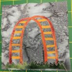 This quilt block is another in the park series, with a green jagged piece of cloth at the bottom to indicate grass. On top of the grass is a giant arch, presumably made out of painted metal/plastic. There are two bars in an arch with bars going between the two that you can climb on. The whole thing is yellow and a splotchy almost rust orange.