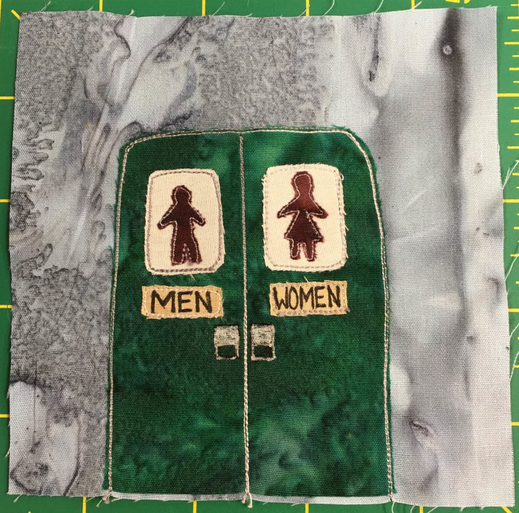 This quilt block shows two big green double doors against a gray background. Due to the background being like the other quilt blocks, this is probably a port-a-potty. On one side is a sign with the silhouette of a man and underneath it it says,