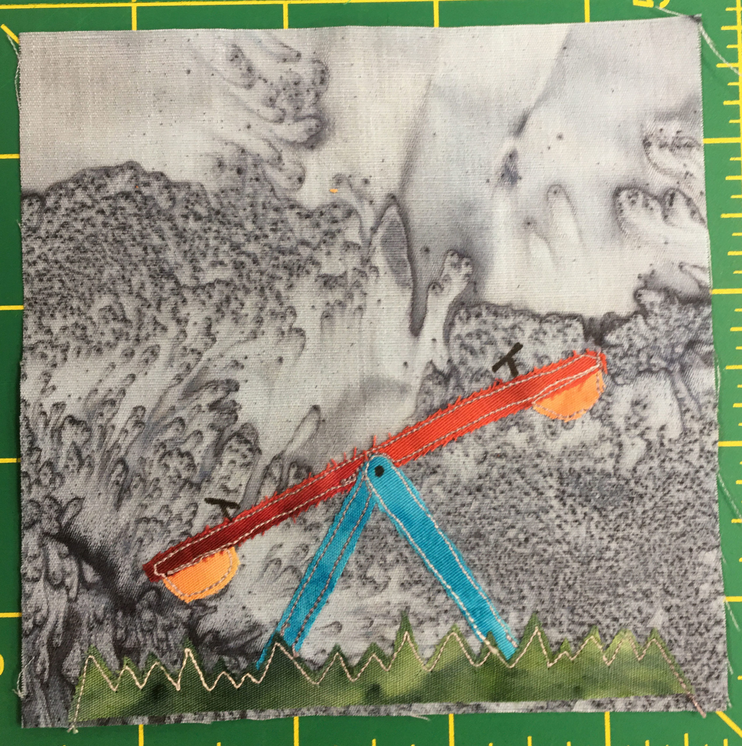 This quilt block shows a see-saw or teeter-totter from the side. This supports are in a light blue fabric, while the see-saw itself is the same burnt orange the other playground equipment was in. On the bottom of each end is a yellow