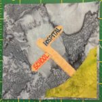 This quilt block shows a corner block, with a patch of bright green grass in the lower right corner. On the patch of grass is a light tan sign post with two signs sticking out in opposite directions. The signs are planks with pointed ends and read, 