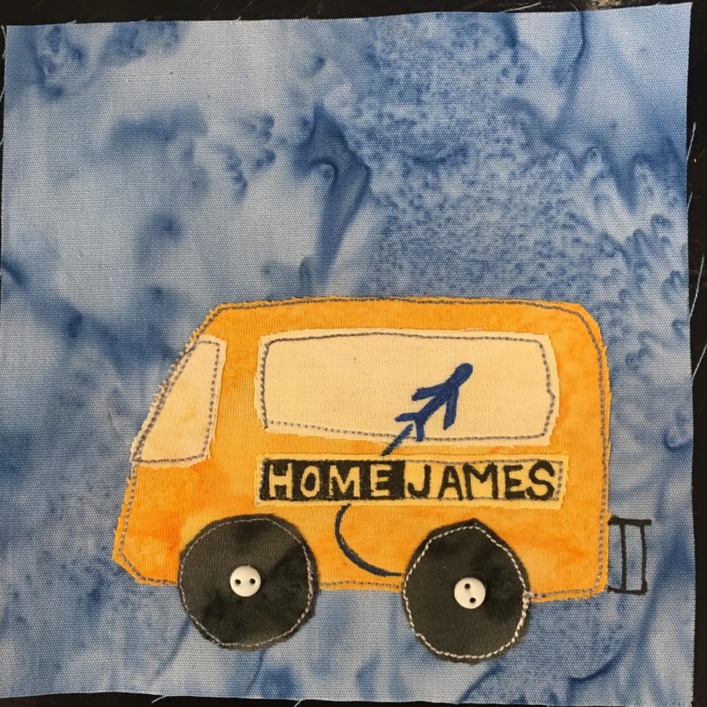 This quilt block shows a yellow airport shuttle against a lighter blue salmon-patterned background fabric. The shuttle is rectangular shaped with a slightly outward curved front (on the left). The windows and windshield are a lighter yellow fabric. On the side, in pen, are the words,