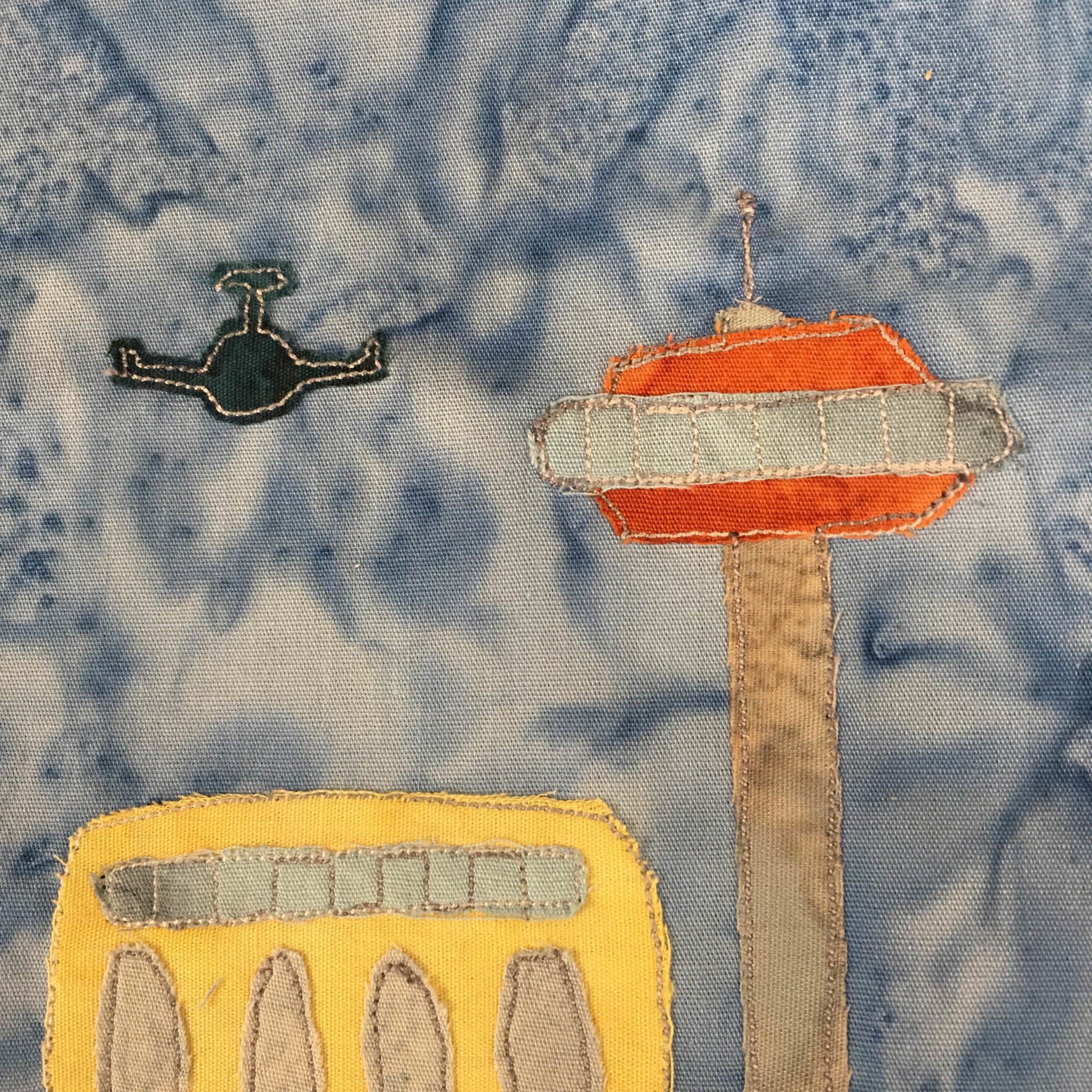 This quilt block shows a dark blue airplane flying over a yellow building with gray windows next to a tall tower topped with an orange windowed capsule and antenna: the air traffic control tower. There is white stitching around the dark blue airplane. The control looks like a Jetson's version of the Seattle Space Needle. This is all against a light blue salmon-patterned background.