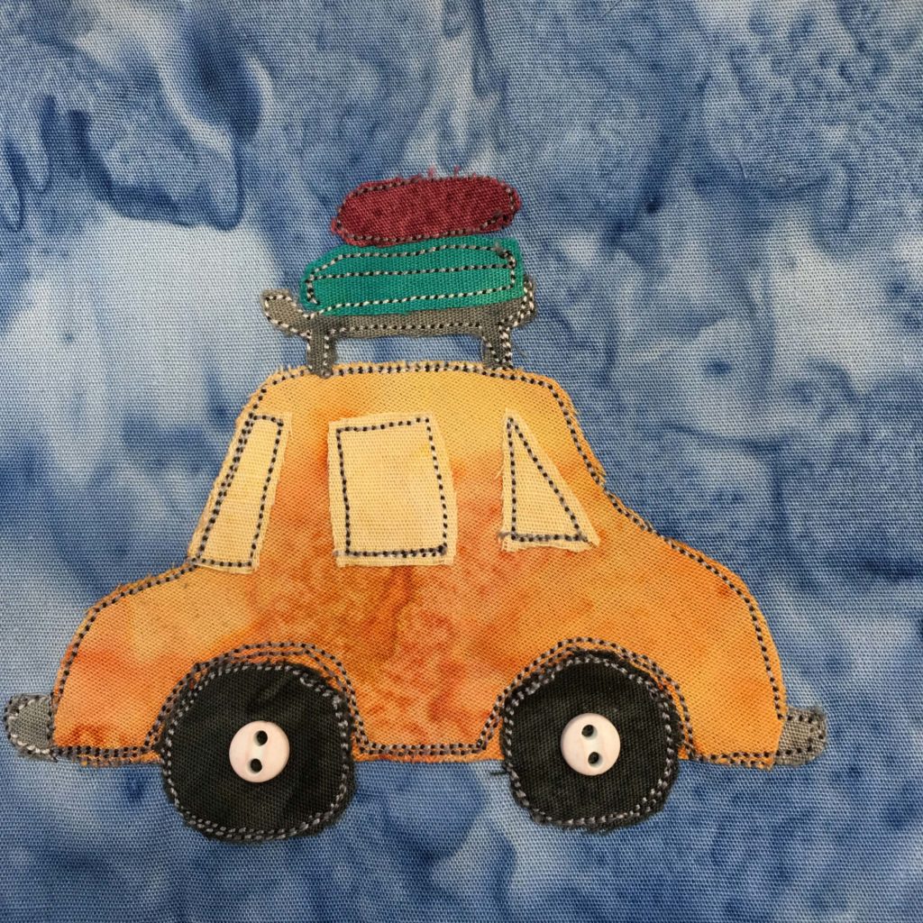 This quilt block shows a yellow sedan form the side with luggage on the rack on top of the car. There is a deep red suitcase and a green suitcase. The car itself has a rear window, a windshield, and a middle window since it's just a two door. Each element is outlined in a dotted black stitching. There are two black tires in the wheel wells and on each tire is a small ivory two-holed button indicating the axle. This is all against a blue salmon-patterned background.