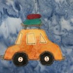 This quilt block shows a yellow sedan form the side with luggage on the rack on top of the car. There is a deep red suitcase and a green suitcase. The car itself has a rear window, a windshield, and a middle window since it's just a two door. Each element is outlined in a dotted black stitching. There are two black tires in the wheel wells and on each tire is a small ivory two-holed button indicating the axle. This is all against a blue salmon-patterned background.