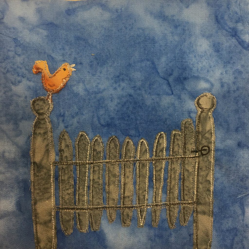 This block shows a metal gate with metal slats across it against a blue background. The gate itself has a little latch top open and close it. Each slat is gray and outlined with a light stitching. On each side of the gate is a post with a round spherical top. On the left post is an orange-yellow bird chirping.