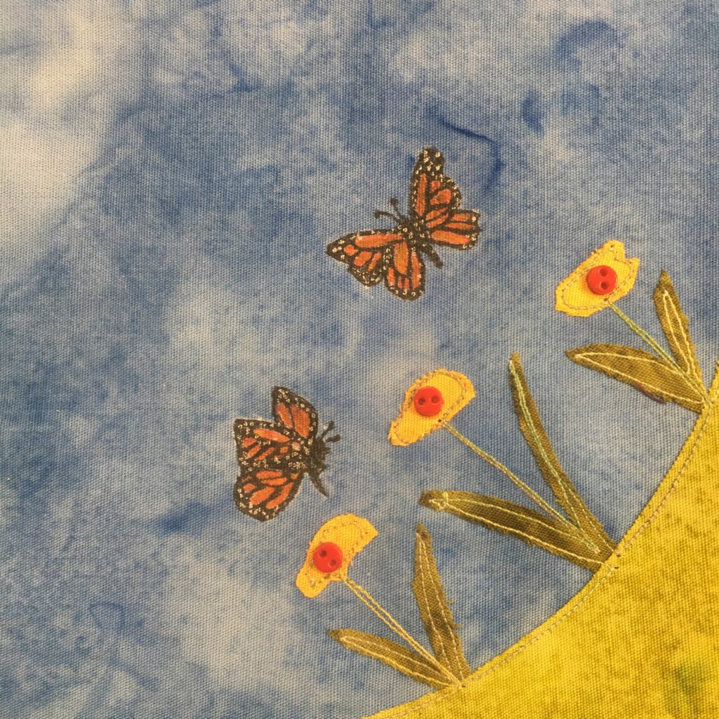 This quilt block shows a corner of grass as a light green fabric in the lower right corner. On this patch of grass are some simple two leafed flowers coming out of the ground. The leaves start at the base and go off to each side. The stems are stitched in and end in a yellow-green bulb. Inside each bulb is a small red two-holed button indicating the pistle. Above the flowers are two butterflies, each a dark spotted black and orange. They are quite the details drawings.