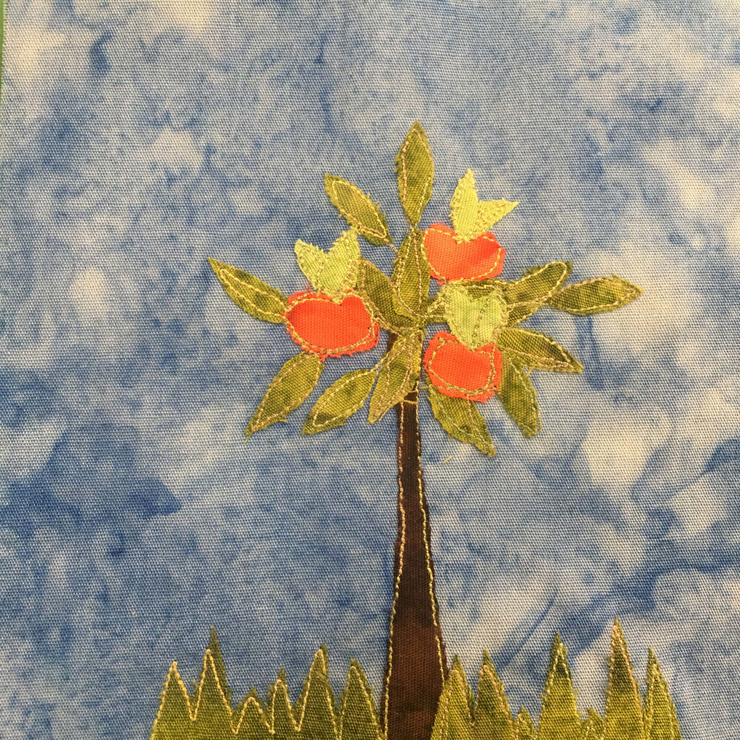 This quilt block shows an apple tree. Much like the previous orange tree there are jagged shaped patches of grass at the bottom of the block. Then there is a trunk that is dark brown and lined by yellow stitching. At the top are many scattered leaves and large round reddish-orange apples. Each apple has a light green stems and leaves sticking out of the top. This is all against a blue salmon-patterned background.