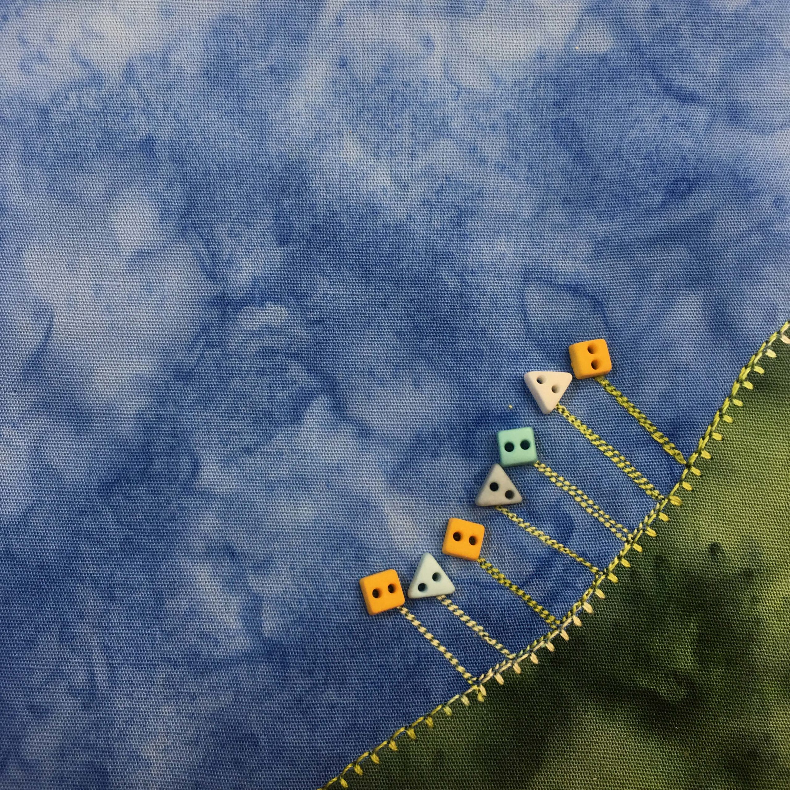 This quilt block shows another corner of grass. This grass is much darker green but it does have the same bold and dashed yellow stitching on the upper border. On top of the dark green grass are stitched lines going up forming stalks of flowers. Each flower ends in a square or triangle-shaped button of varying colors (yellow, blue, gray). These buttons are very small.