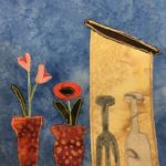 This quilt block shows a shed on the left side, and some tools on the side (front to us) of the shed. There is a gray pitchfork, and a light gray shovel. The shed itself is a piece of light tan orange fabric, with a dark brown roof that has yellow stitched outline. On the left side of the block are two potted flowers. The pots are a dark red with lighter duotone polka dots. The two flowers are different, one having two bulbs that are pink and red, and one being sunflower-like with a red outside and a black center.