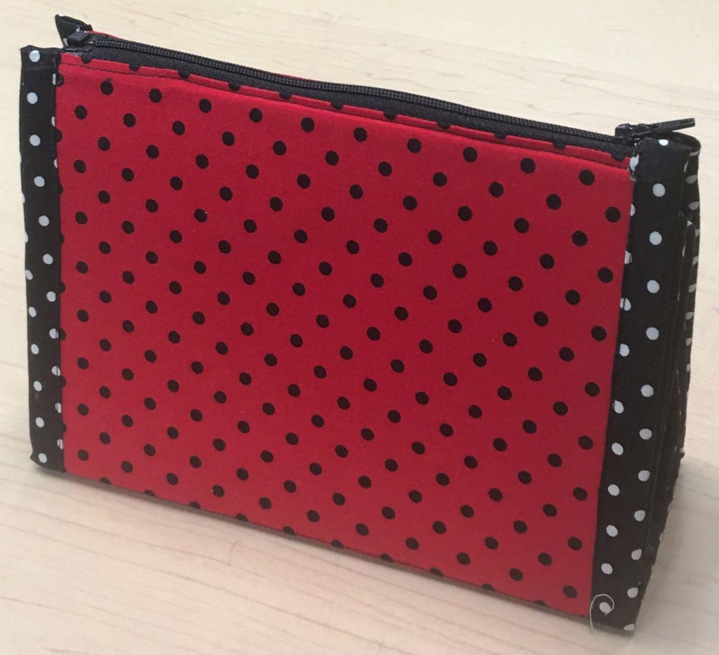 A red-polka dotted pouch standing up right and zipped shut.