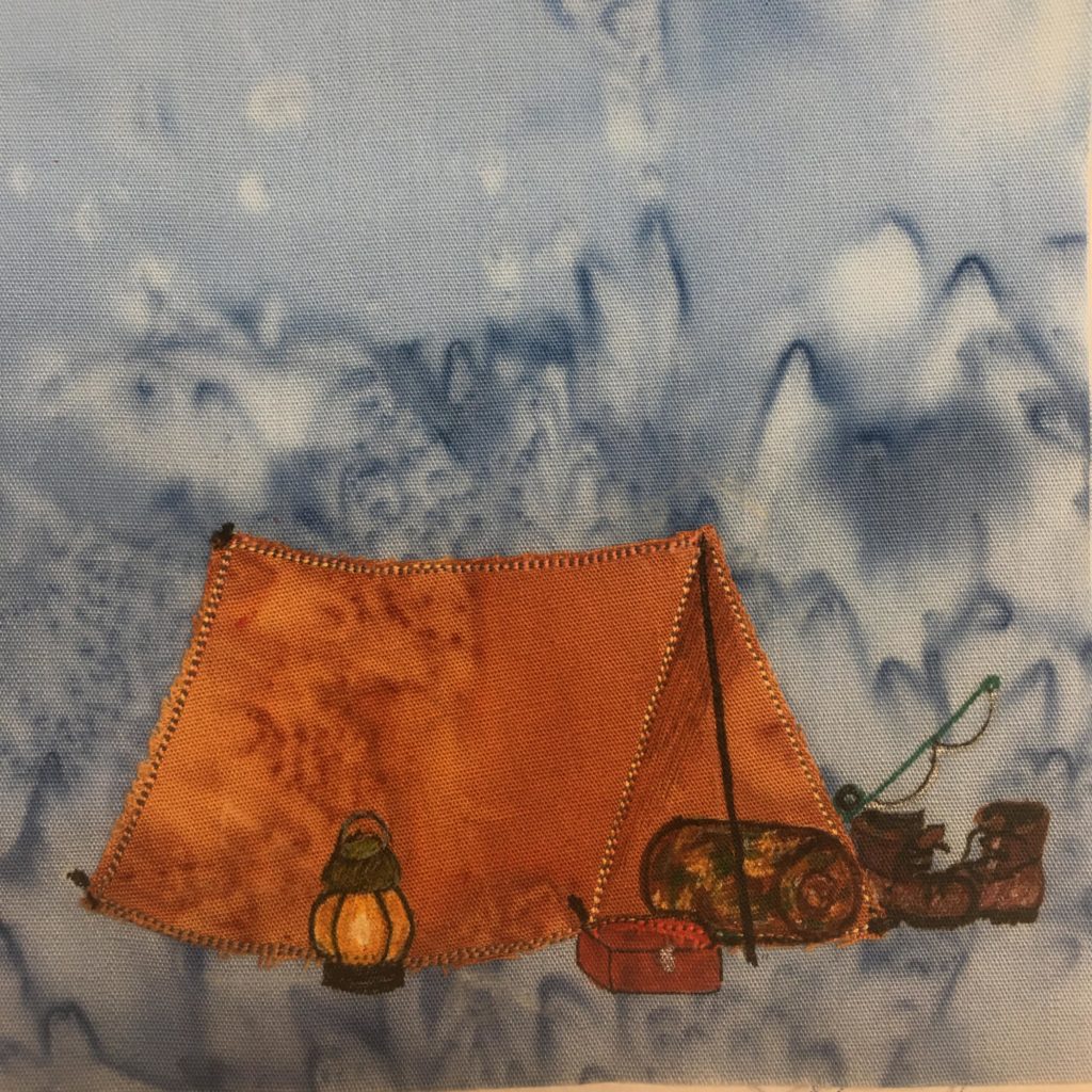 This quilt block shows an orange tent. It's a simple set up tent with two poles holding up a center rail that a blanket is laid over. There are brown steel toed red wings drawn in pen to the right side of the entrance of the tent. There's also a fishing pole above them drawn in. At the entrance of the tent is a camouflage sleeping bag rolled up (with pen markings for the camouflage). Next to the that is a red tacklebox that is drawn in with red pen. And finally to the left next to the orange tent is drawn in a lantern. This is all against a blue salmon-patterned background.