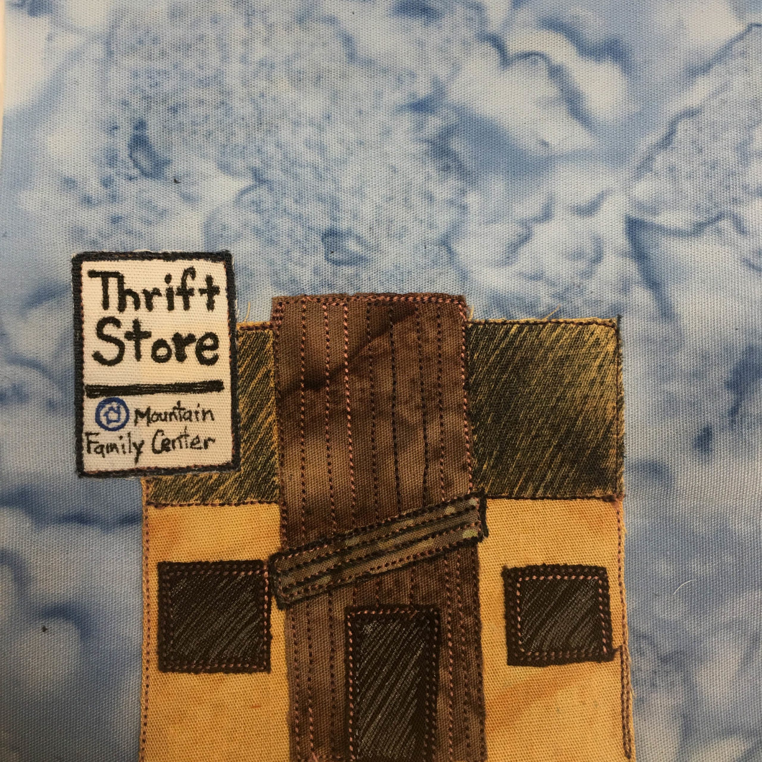 This quilt block shows a square building of brown and yellow. In the upper left is a large sign that protrudes farther than the building's edge. It's white and on it are the words,