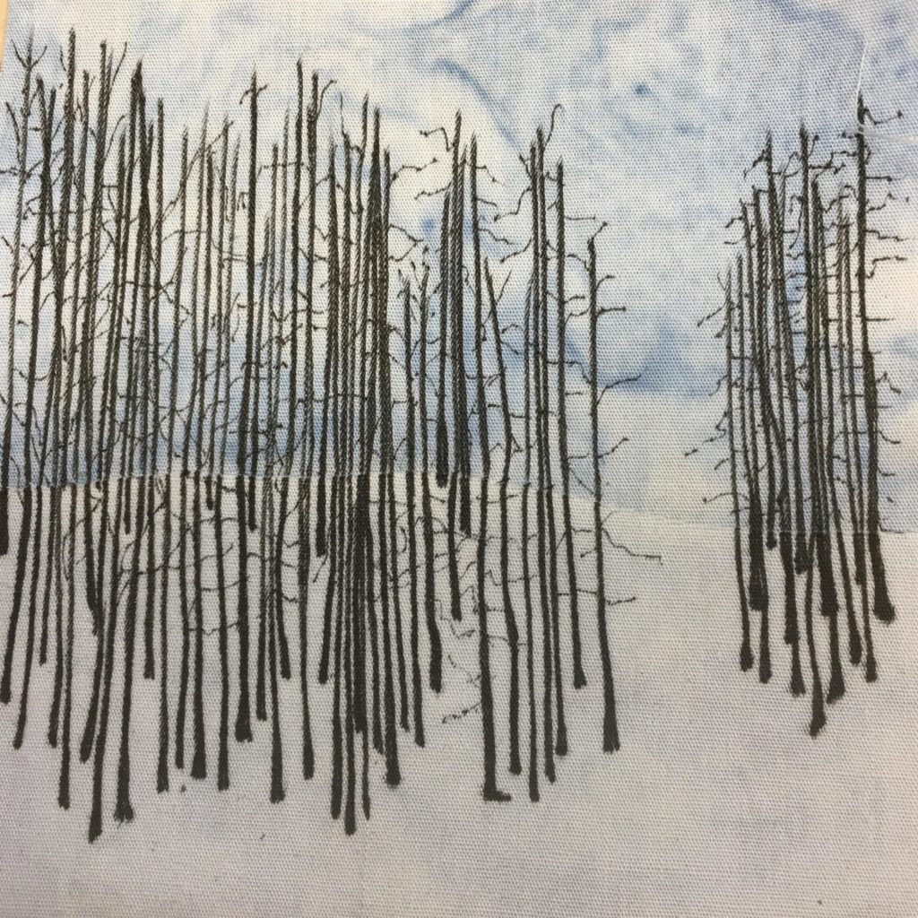 This quilt block shows a blue salmon-patterned background with a bunch of very thing black vertical lines on it. The vertical lines have a larger base at the bottom of them. These are dead trees with little black skeletal like branches coming off them. There are dozens and dozens on this block making up a quite burnt forest.