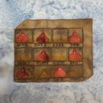 This quilt block shows a brown piece of fabric made to look like a big rectangular box on its side with demarcated boxes in pen in it. In each box is either yellow hay, or a light rust colored hen sitting on eggs looking at the viewer. This is against a blue splotch background fabric.