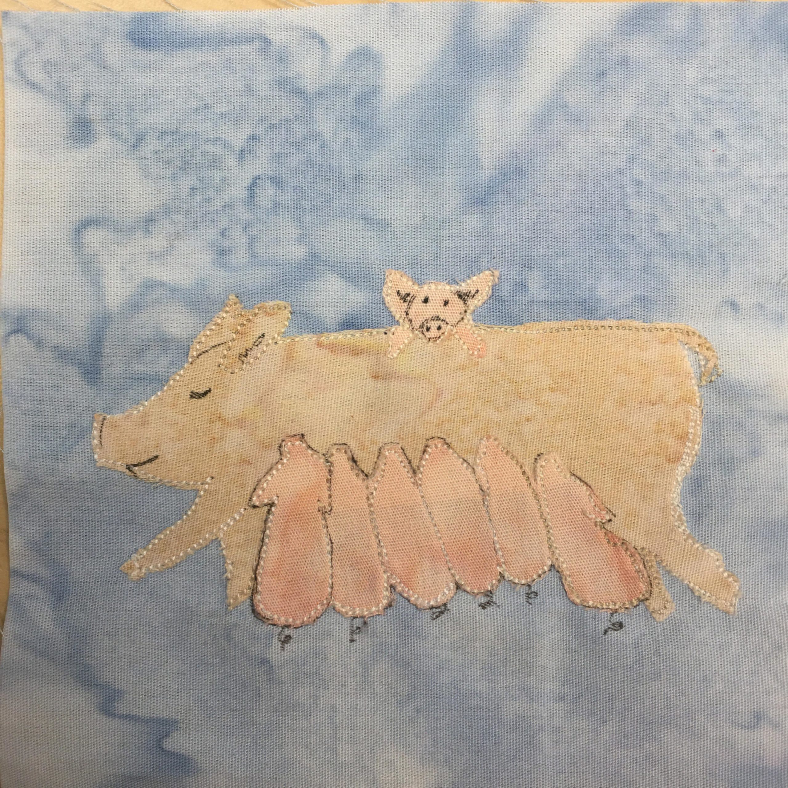 This quilt block shows a bunch of pigs against a blue background. In the center of the block is a light skin colored large sow lying on her side. Underneath the sow are six pink piglets curled up and suckling on her. There are little curly-q tails at the end of each. On the sow's back is single pig facing the camera with his little two front legs visible. His face is drawn in with a black pen.