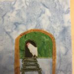 This quilt block shows a hen house against a blue salmon-patterned background. The hen house is up off the ground, held up by a light brown arch. The front of the hen house is green, and the ladder/stair going up into the house is a dark green. Inside the hen house, on the black arch of the entrance is a white chicken made of white fabric. There is a red markings for the head. The stitching outlining each part of the hen house is a golden yellow color.
