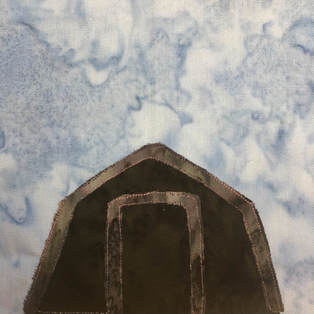 This quilt block shows a very dark, practically black, pentagon shaped shed on the lower half. It has a lighter grey frame on the outside and around the door. It is against a salmon-patterned blue background.