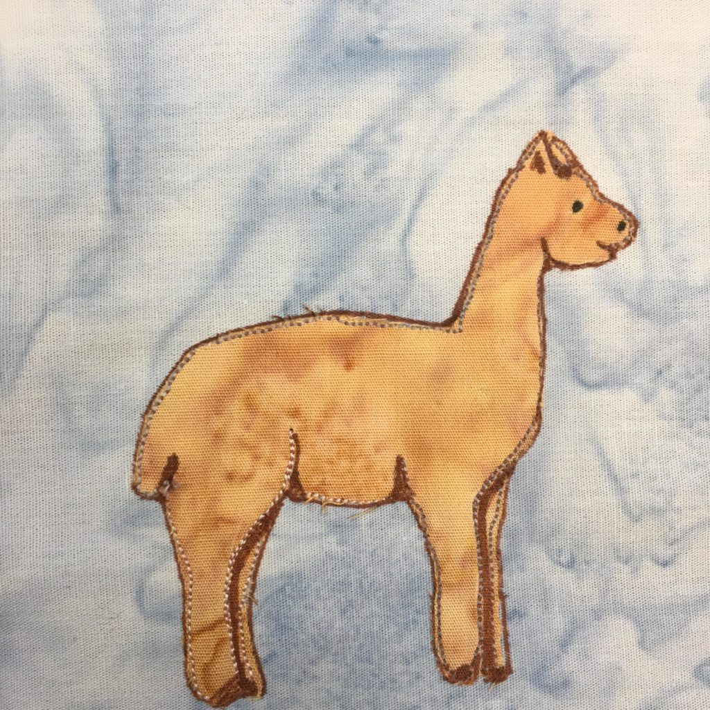 This quilt block shows a llama standing from the side. The llama is pointing to the right. It has a stocky build, with thick legs and a thick neck. It's tall neck goes up to a head you might think was smiling. There is a dot for the eye and some penning in to indicate the ears. The llama is made up of one big piece of tan fabric with stitching and penning ot indicate the various contours of the body (such as the legs). This is all against a blue salmon-patterned background.