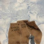 This quilt block shos three grain sacks made up of brown piees of fabric. Each sack has a black pen writing that says,