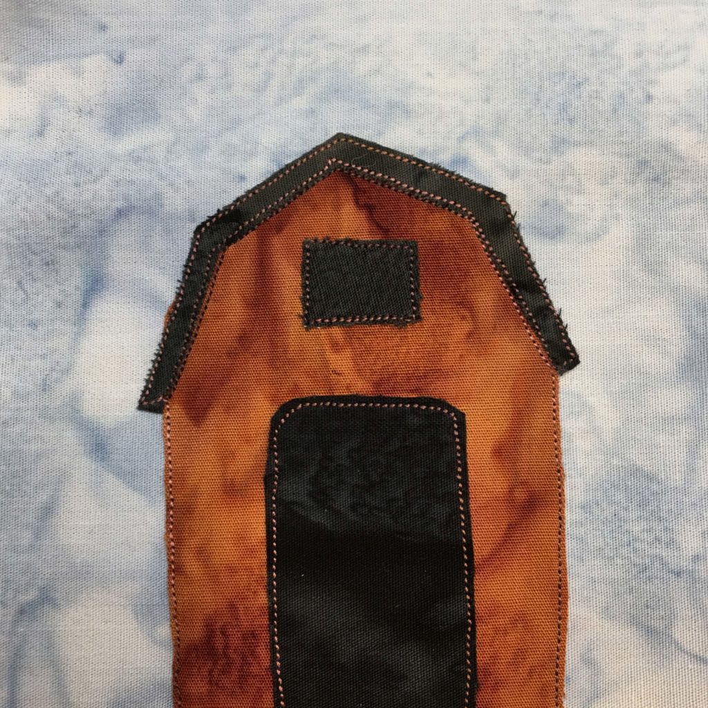 This quilt block shows a simple deep orange barn. It's very tall and has a tall and wide black opening for the entrance. The loft has an opening as well like a black window. The angular roof is also black.