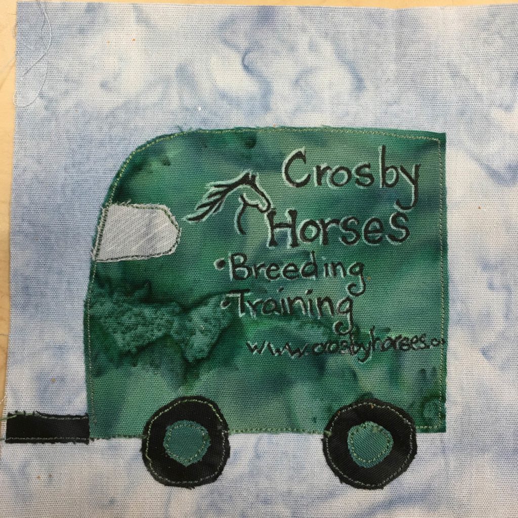 This quilt block shows the trailer attached to yesterday's SUV. The trailer is the same tint of green that the SUV was, which is a darker green. On the side is a big logo written in black and white pen (white to highlight the outlines) that shows a horse head and neck and the text, "Crosby Horses • Breeding • Training www.crosbyhorses.com" There are two sets of wheels on the trailer, despite it's short length, which are black with green axles. There isalso a window on the upper front of the trailer which is a white fabricwith white pen lines showing the reflection.